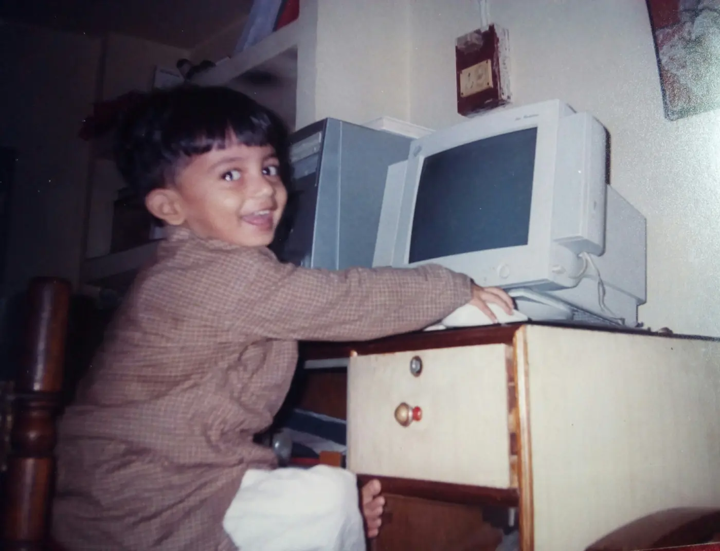A young Basharat grinning over his shoulder from a chair at an old beige computer